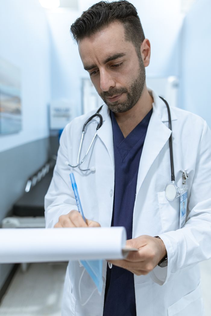 Offerings A male doctor writing in a medical chart in a hospital hallway.