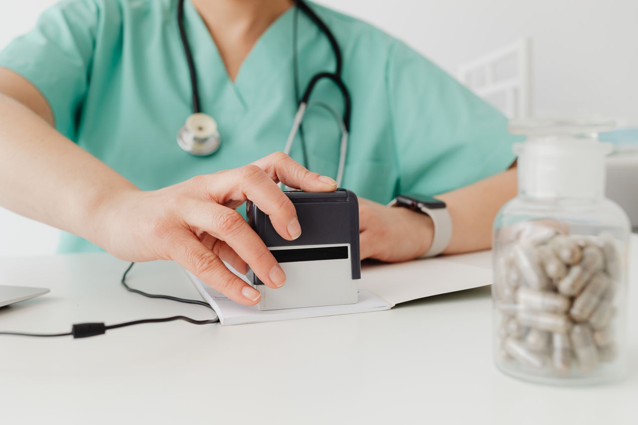 Offerings Close-up of a doctor stamping a prescription with a bottle of pills on a desk.